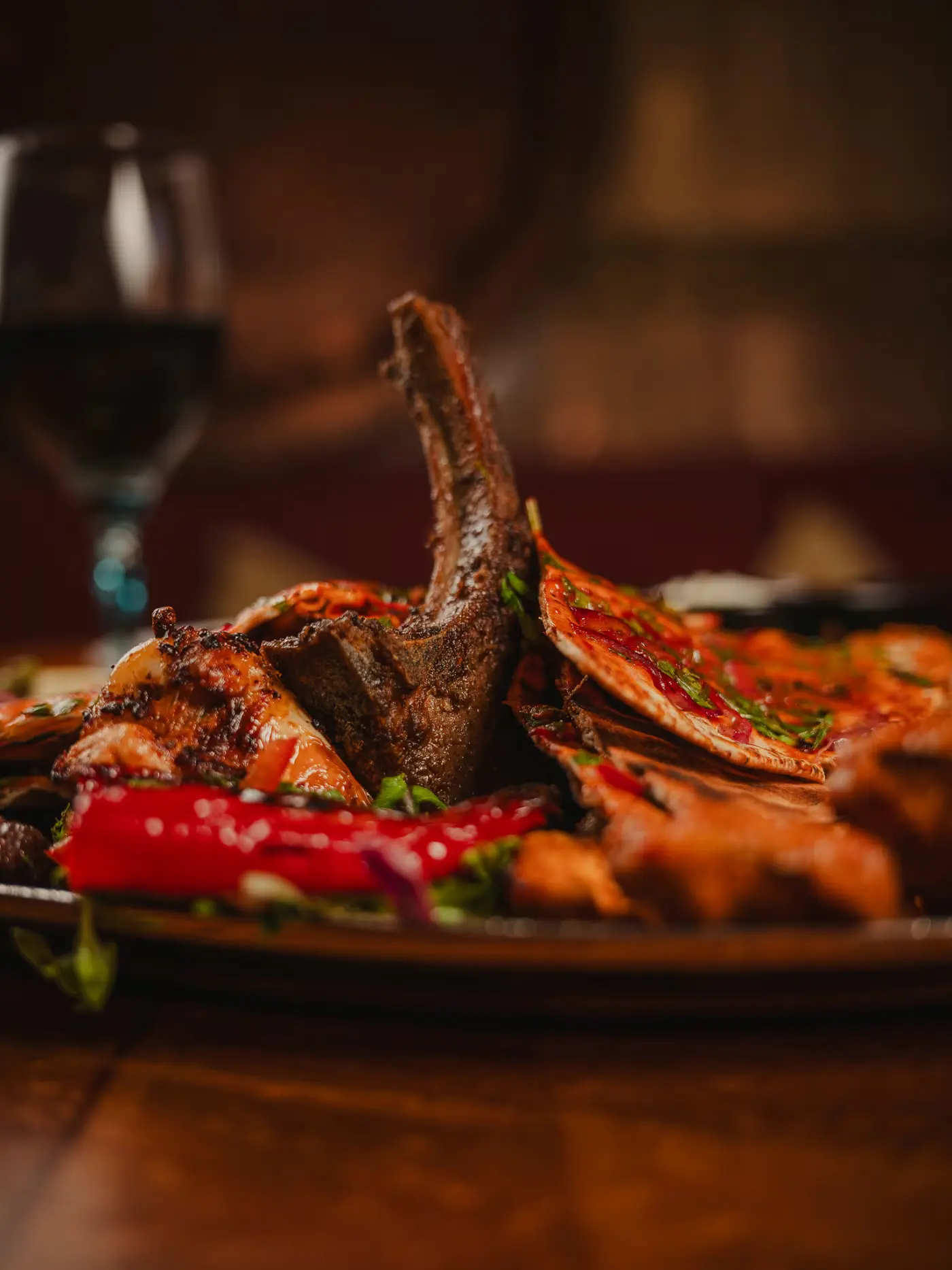 Lamb chops and grilled pepper in moody candlelight beside a glass of red wine at Beirut Restaurant. Food photography by Gorka Di Capitan (gorkadicapitan.com).