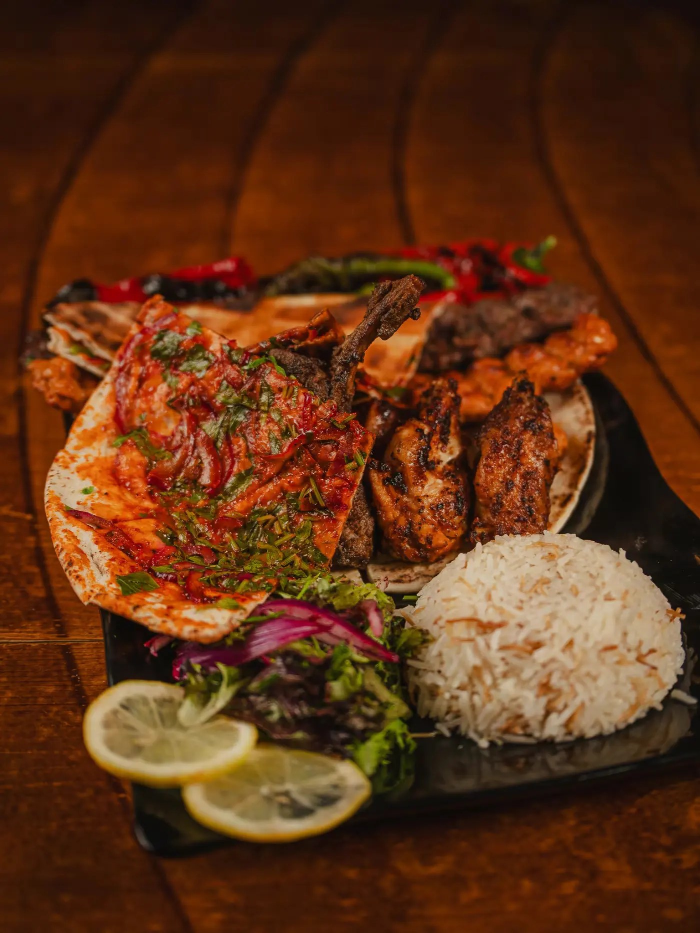 Grilled chicken, lamb chop and kebab on flatbread with tomato sauce, rice, salad and lemon on a black plate at Beirut Restaurant, food photography by Gorka Di Capitan (gorkadicapitan.com)